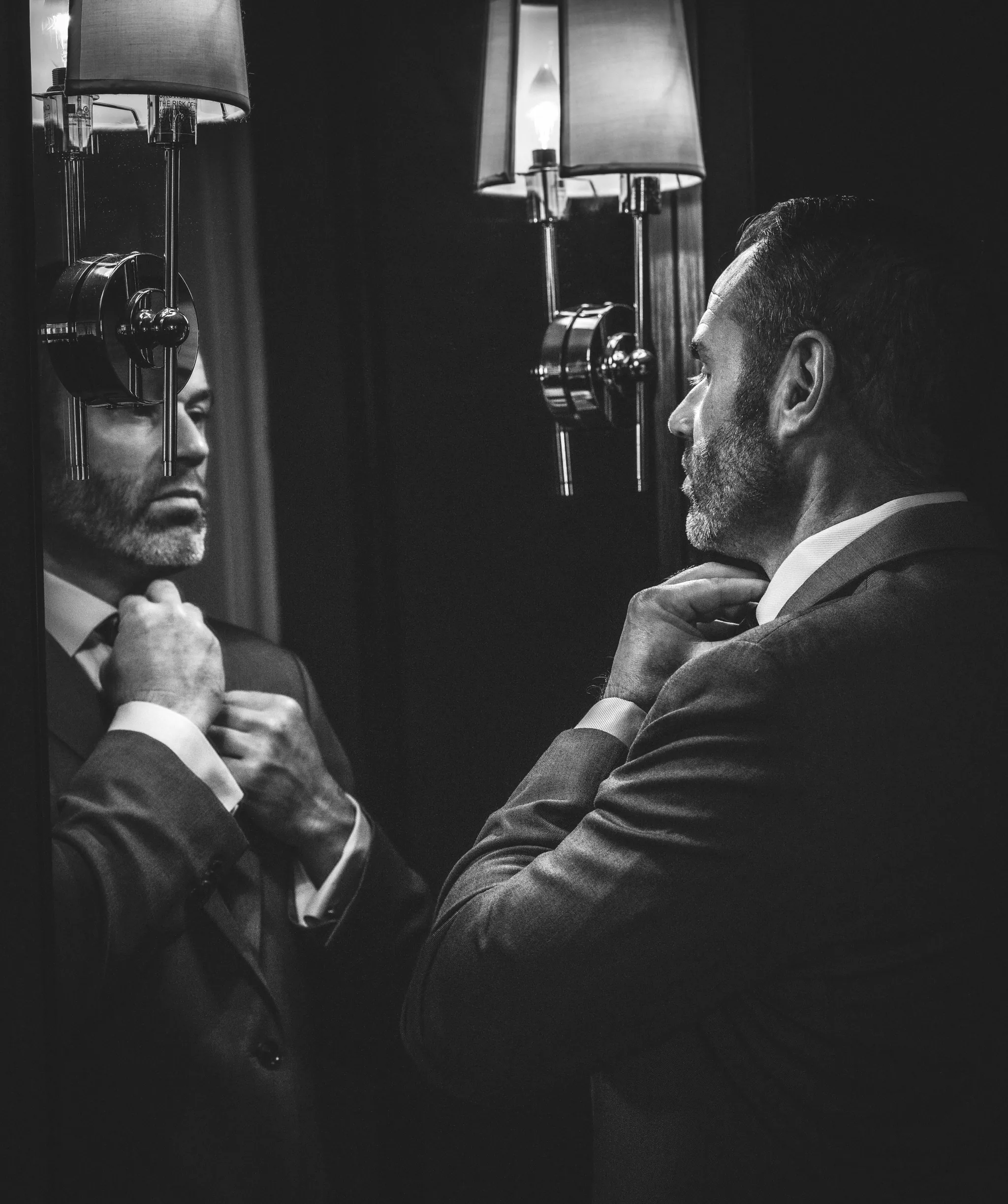 black and white portrait of a man in a suit looking in a large mirror