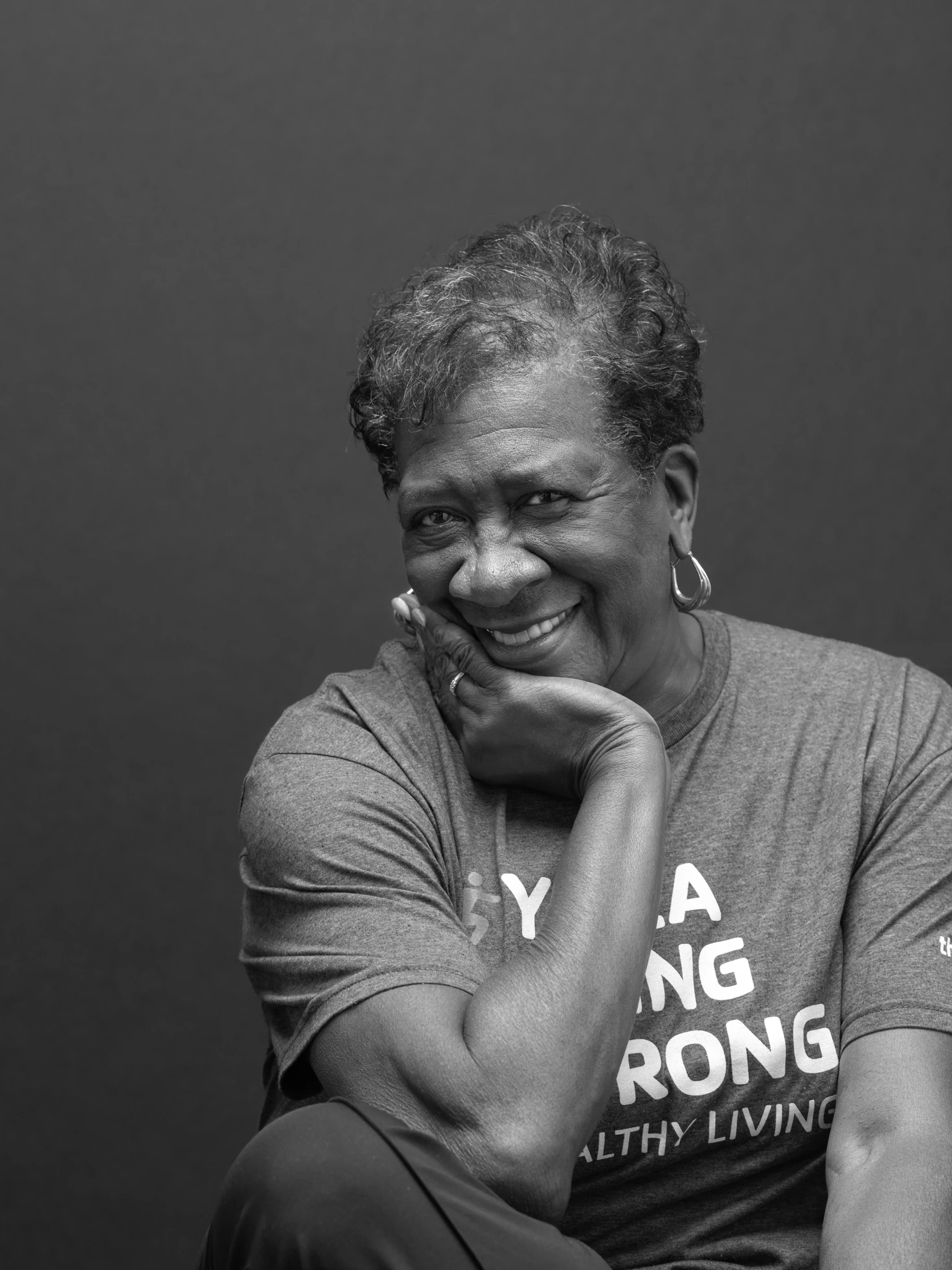 black and white studio portrait of a senior woman smiling chin in hand very relaxed